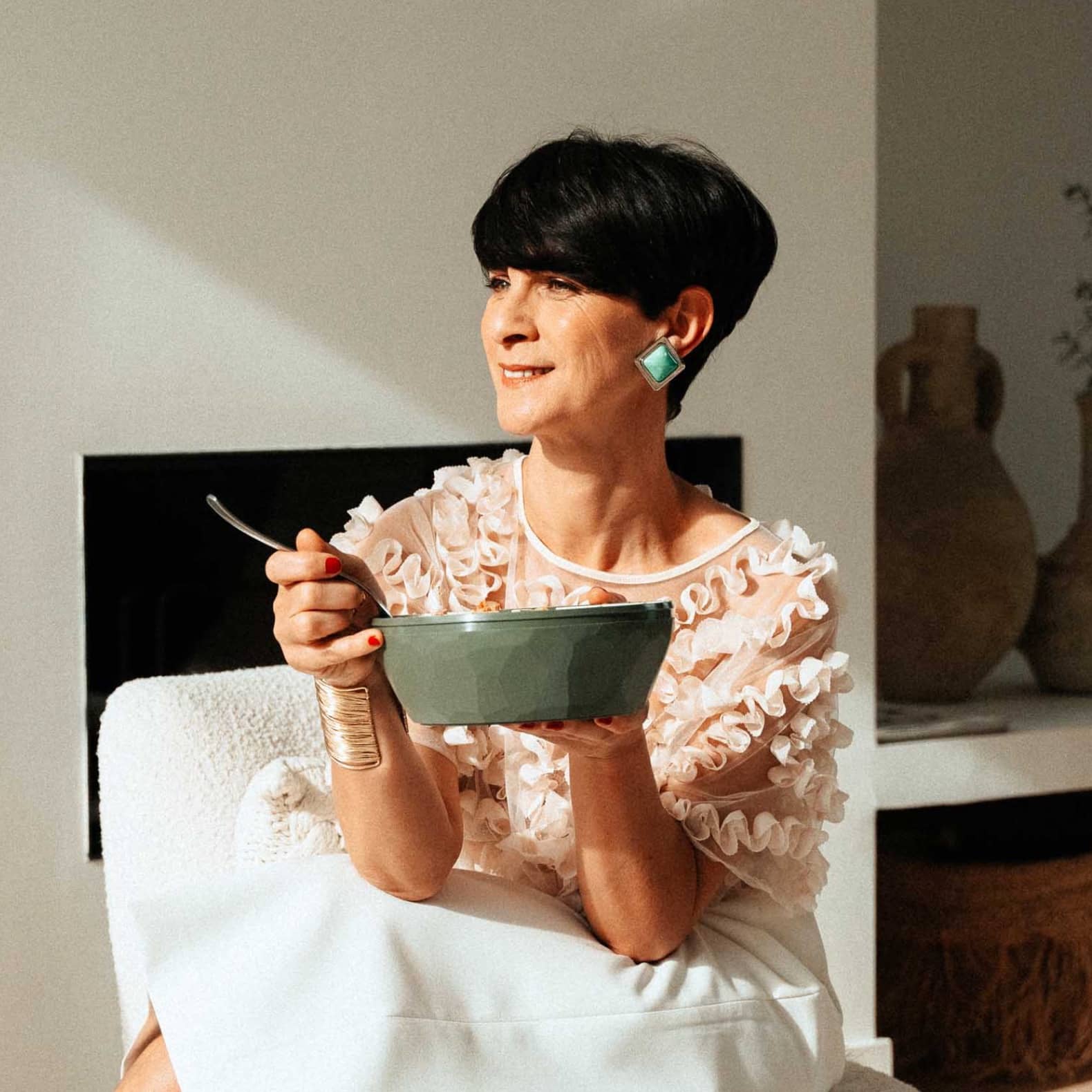 Femme regardant au loin, et tenant un bol maju de couleur kaki dans la main.