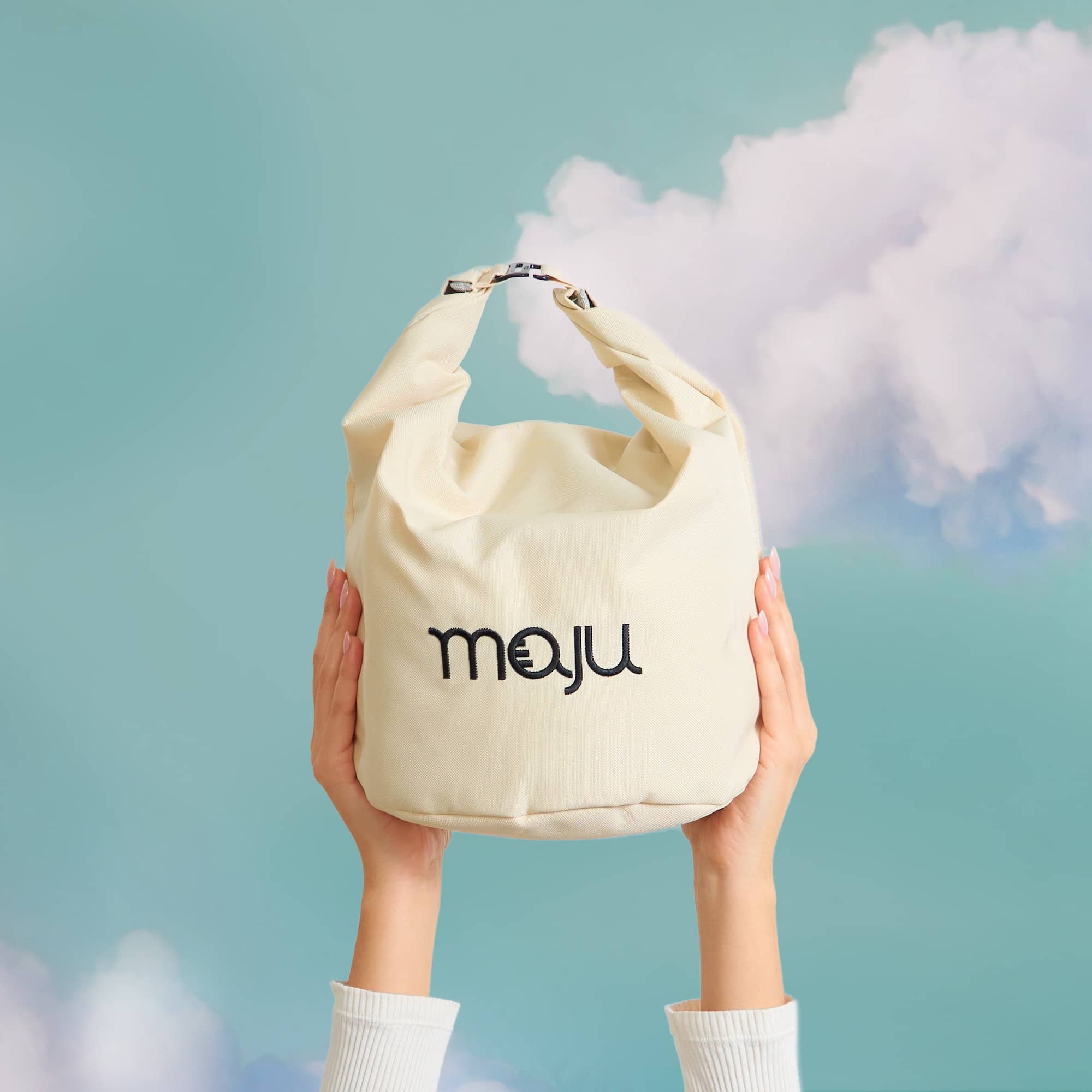 Sac isotherme maju de couleur beige porté en bout de main, sur fond nuage.