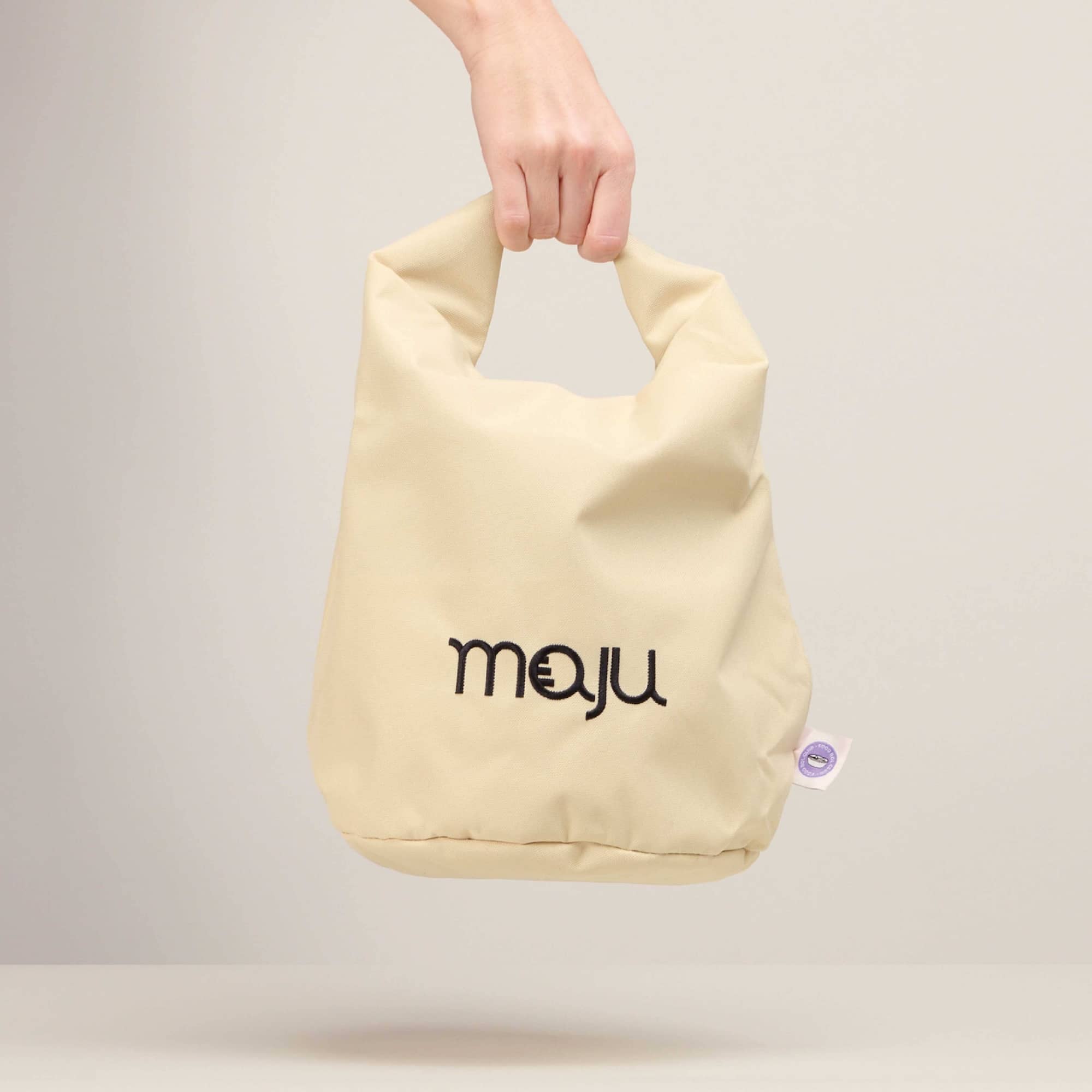 Sac isotherme maju de couleur beige maintenu par la main.