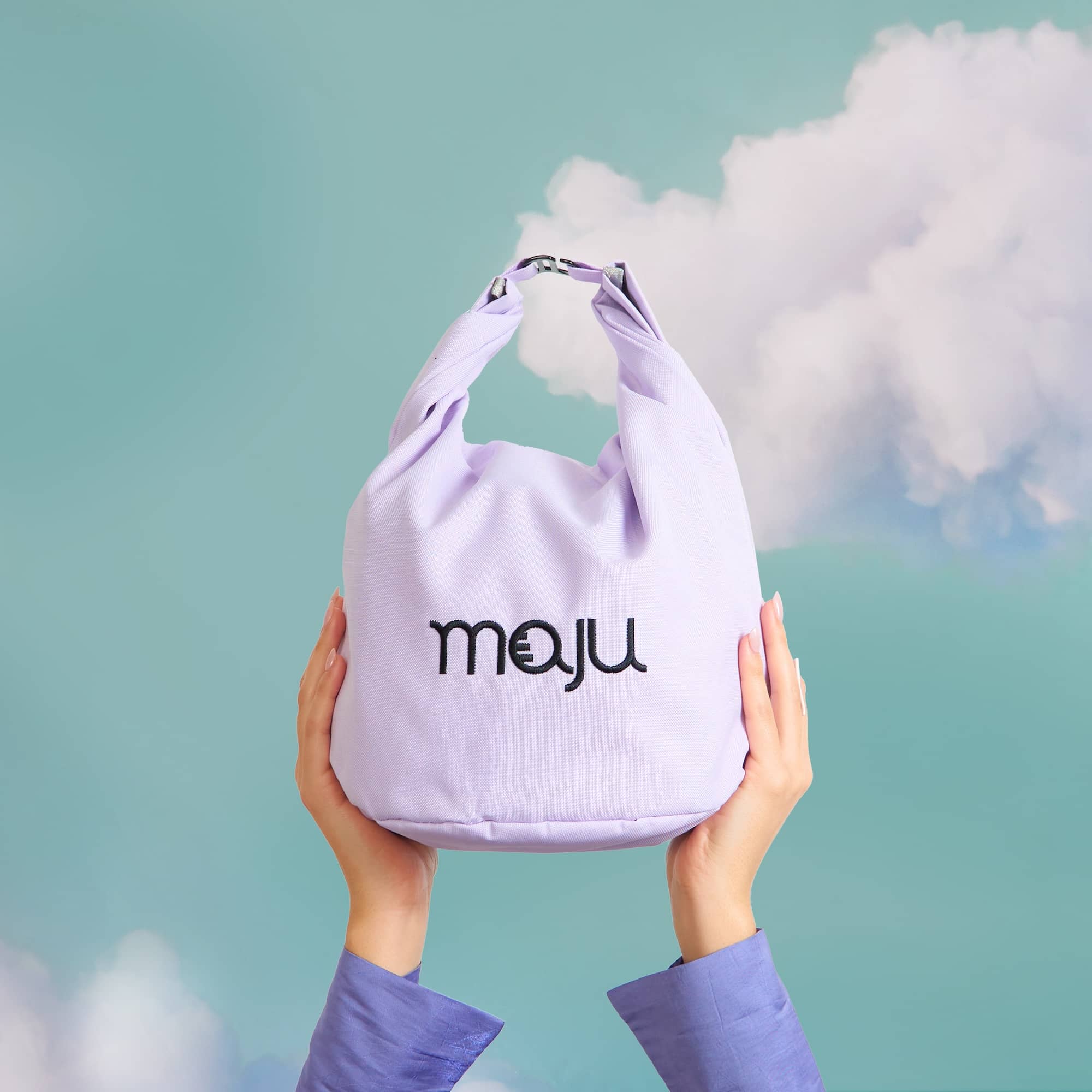 Sac isotherme maju de couleur violet porté en bout de main, sur fond nuage.