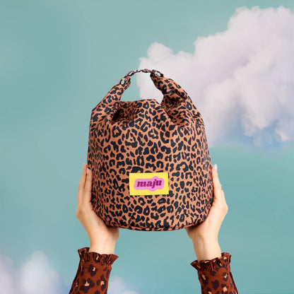 Sac isotherme maju de couleur leopard porté en bout de main, sur fond nuage. 